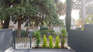 Une cour avec un sol carrelé, une porte en métal et diverses plantes.