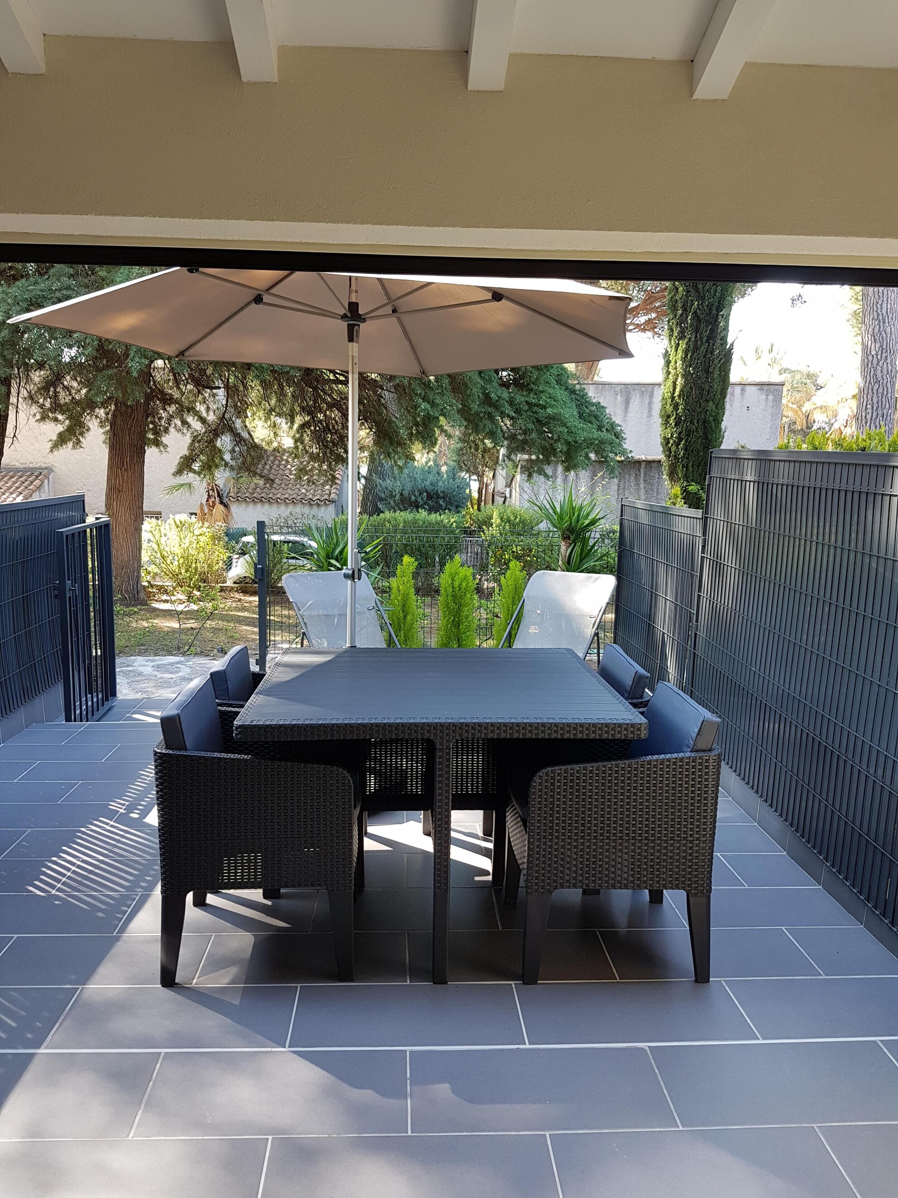 Un patio exterior con mesa y sillas, una pérgola y vistas a un jardín y árboles.