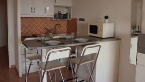 A compact kitchen with white cabinets, a microwave, a sink, and two bar stools.