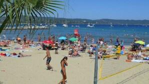 A beach with people sunbathing and playing volleyball.