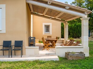 A covered outdoor seating area with a table and chairs, a window, and a wooden planter. - Homerez - Villa in Saint-Saturnin-lès-Apt (Saint-Saturnin-lès-Apt)