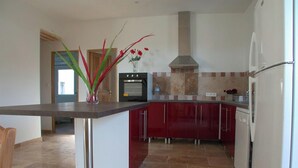 Una cocina moderna con una isla central, armarios rojos, una campana extractora de acero inoxidable y un horno empotrado.
