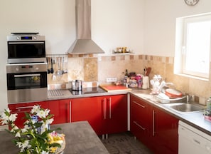 Una cocina moderna con armarios rojos, un horno doble, un lavabo y un ventanal.