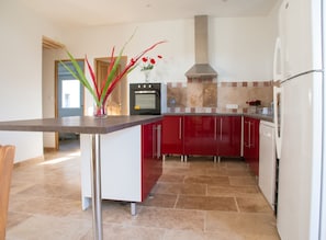 A modern kitchen with a central island, red cabinetry, and a stainless steel range hood. - Homerez - Villa in Saint-Saturnin-lès-Apt (Saint-Saturnin-lès-Apt)