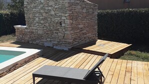 Una terraza de madera con un muro de piedra, una piscina y una silla de descanso.