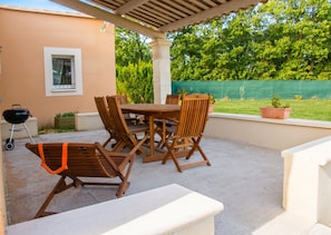 Un patio al aire libre con mesa y sillas, una parrilla y un espacio cubierto.