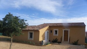 Una casa de un piso con techo de tejas, un porche pequeño y un camino de entrada de grava.