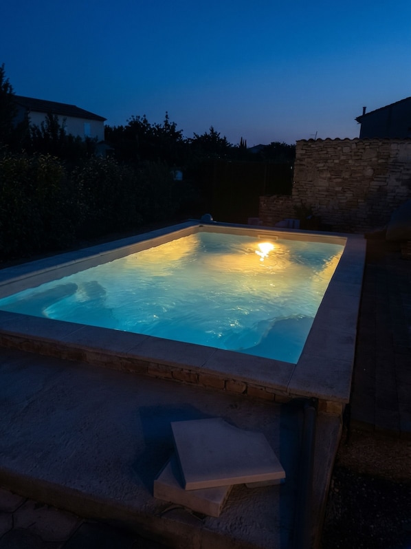 Piscina rectangular al aire libre con borde de piedra, rodeada por un muro de piedra y vegetación.