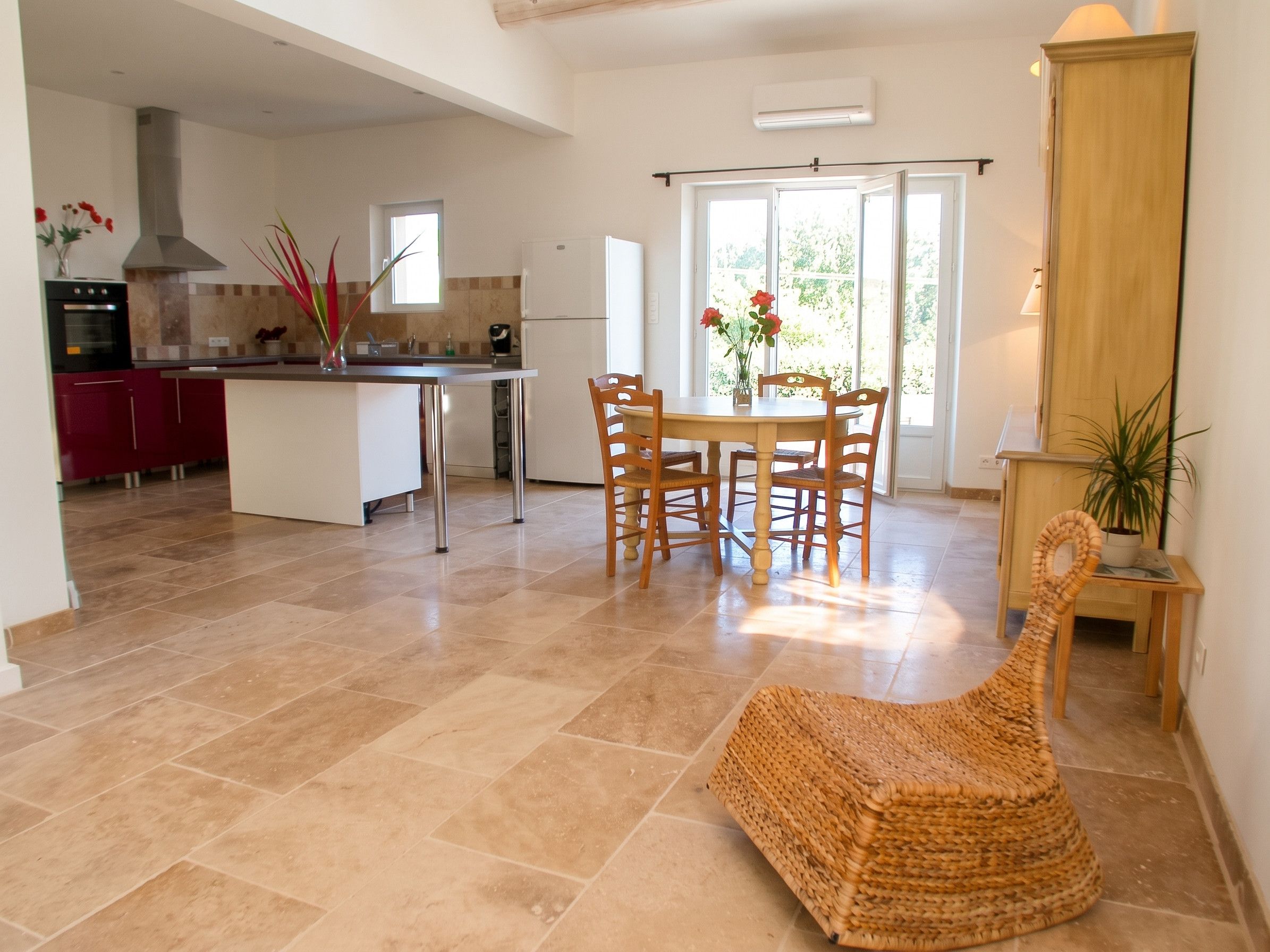 A spacious kitchen with a dining area, a wicker chair, and a view of the outdoors.