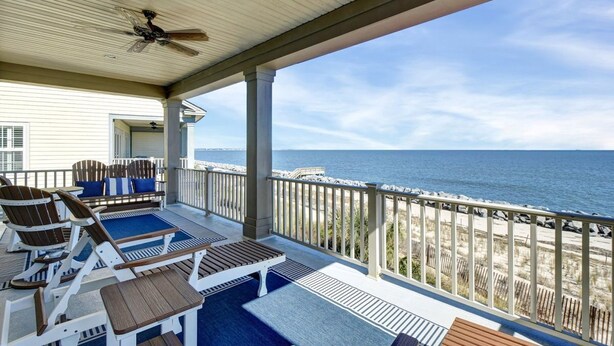A covered outdoor area with Adirondack chairs, a wooden table, and a view of the ocean. - Ocean Cottage 39 Halekulani The Cottages at Jekyll Island Oceanfront (Jekyll Island)