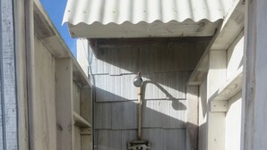 Une douche extérieure en bois, dotée d’un toit en métal ondulé, de marches en bois et d’un pommeau de douche en métal.