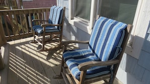 Deux fauteuils à bascule avec des coussins à rayures, placés sur une terrasse en bois.