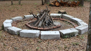 A circular fire pit surrounded by concrete blocks in a wooded area.