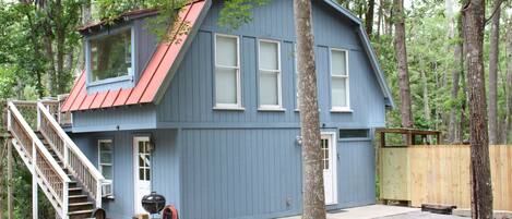 A blue cabin with a red roof, a front porch, and a staircase leading to the entrance.