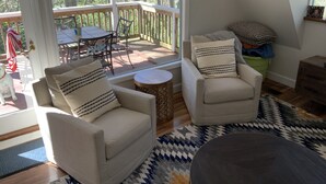 A cozy living room with two armchairs, a small round table, and a view of a wooden deck and trees.
