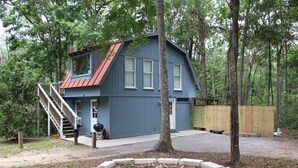 A blue house with a red roof, a wooden deck, and a fire pit in the yard.