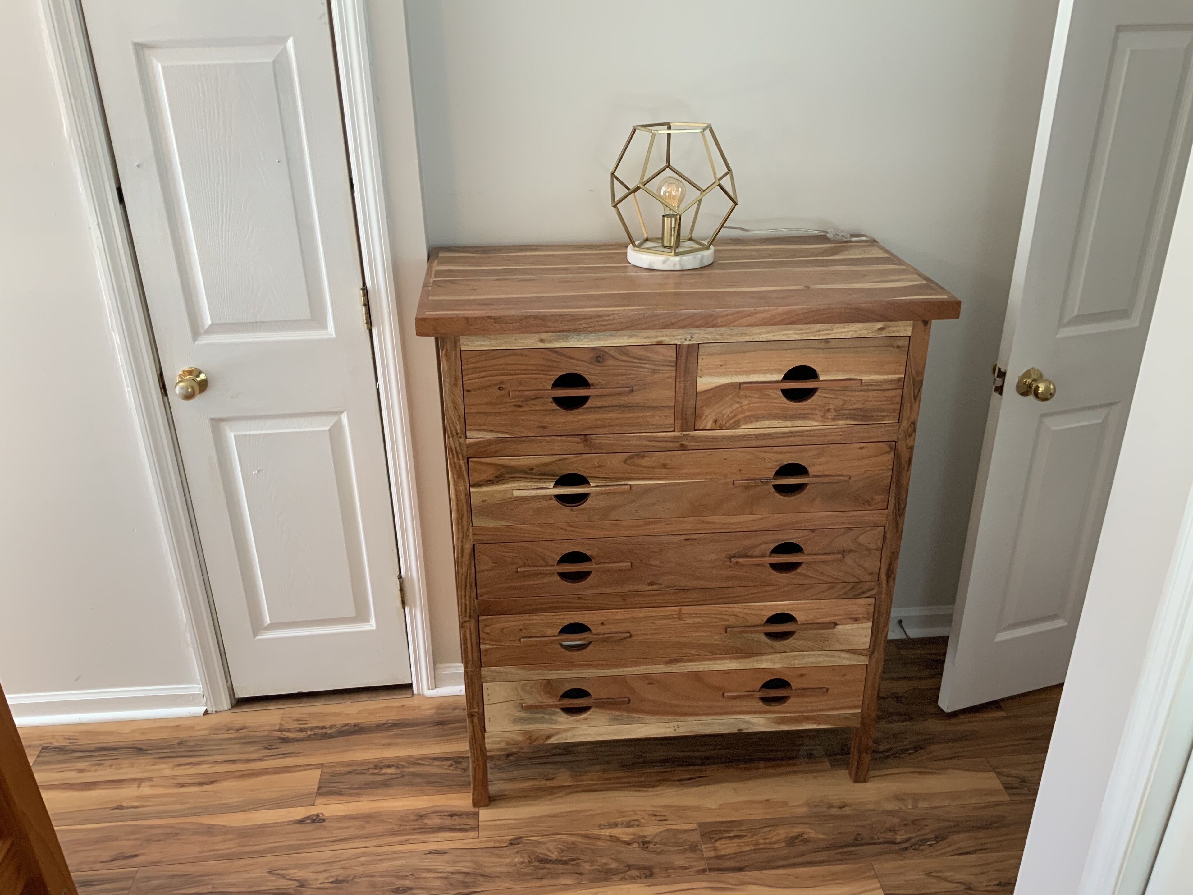 A wooden chest of drawers with multiple compartments and a geometric light fixture on top.