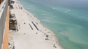 A beach with a long pier extending into the water, a sandy shore with people and umbrellas, and a clear view of the ocean. - Splash Luxury Oceanfront Condo with Master on Gulf! (Panama City Beach)