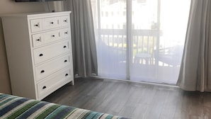 A bedroom with a bed, a dresser, a TV, and a balcony with curtains. - Great Condo With Ocean Views!! (Brigantine)