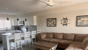 A modern kitchen with white cabinets, a dining area with wooden chairs, a brown sofa, and a ceiling fan. - Great Condo With Ocean Views!! (Brigantine)