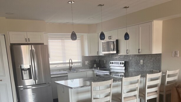 A modern kitchen with white cabinetry, stainless steel appliances, and a central island with seating. - Great Condo With Ocean Views!! (Brigantine)