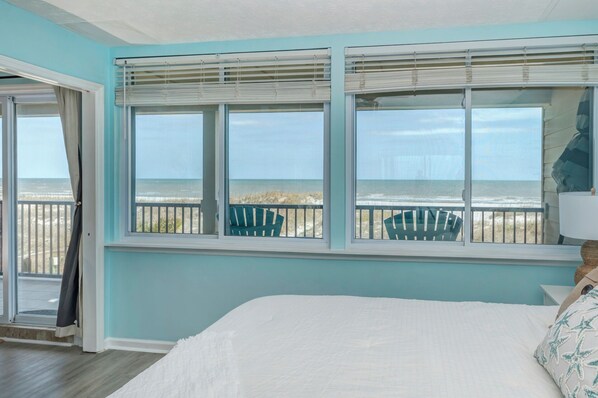 Un dormitorio con vista al mar, una cama y una ventana con persianas.