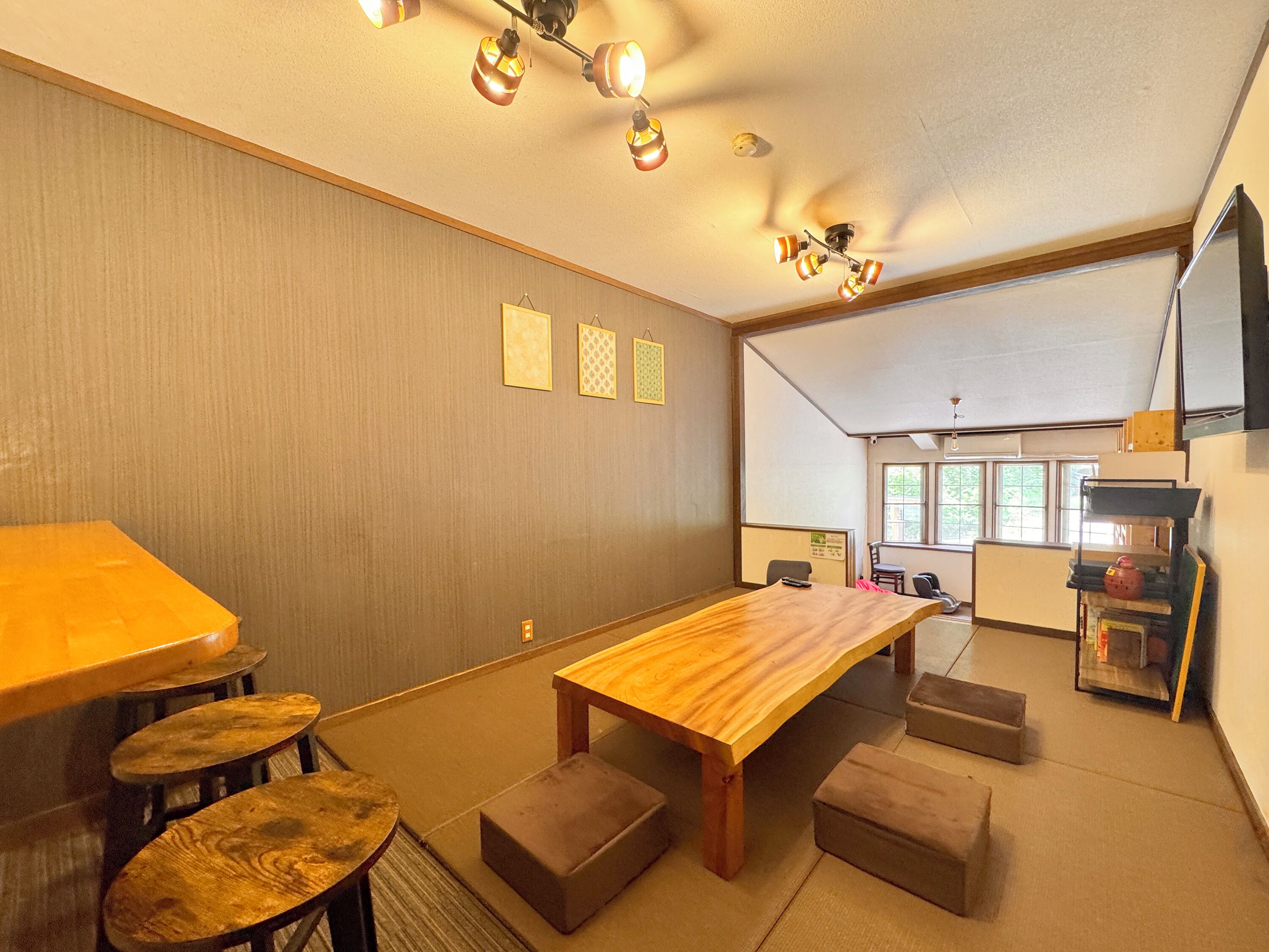 A room with a wooden dining table, cushioned seating, a ceiling fan, and a kitchen area with a refrigerator and sink.