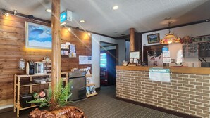 A reception area with a wooden wall, a reception desk, a coffee machine, and a mounted picture. - Pension Kobekko (Otari)