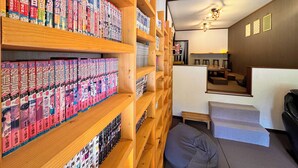 A room with wooden shelves filled with manga books, a small seating area with a cushion, and a staircase leading to another room. - Pension Kobekko (Otari)