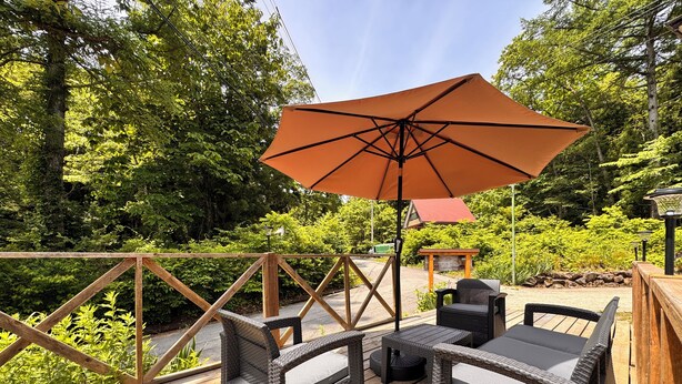 A wooden deck with wicker furniture and an umbrella. - Pension Kobekko (Otari)