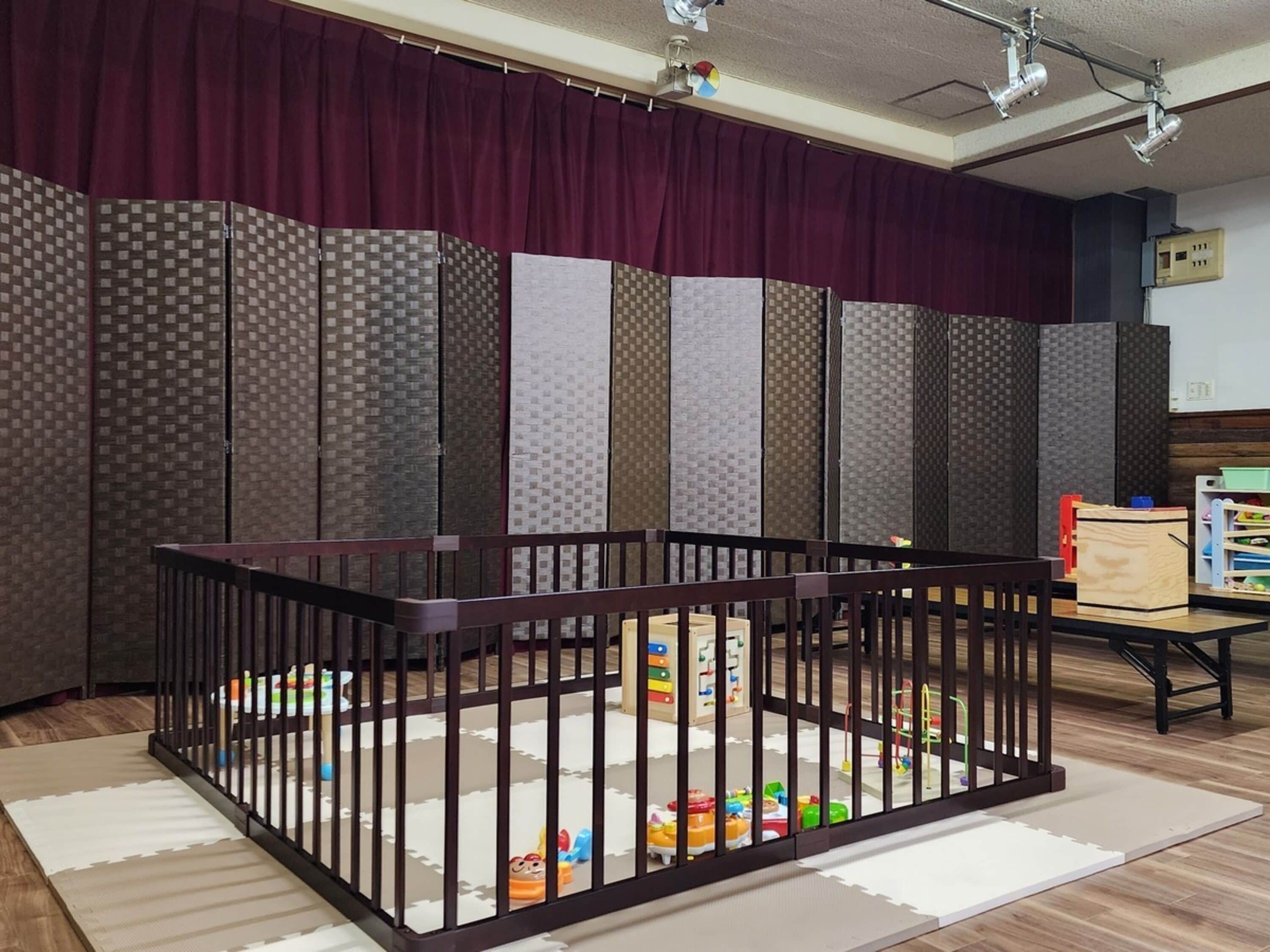 A room with a baby playpen, a wooden cabinet, and a curtain.