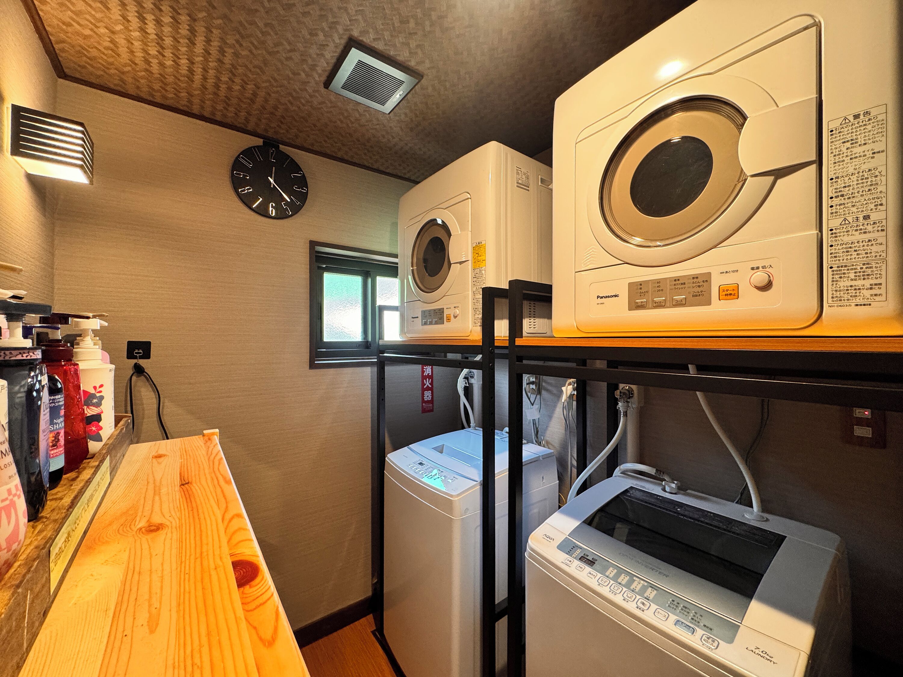 A laundry room with multiple washing machines, a clock, and various toiletries on shelves.