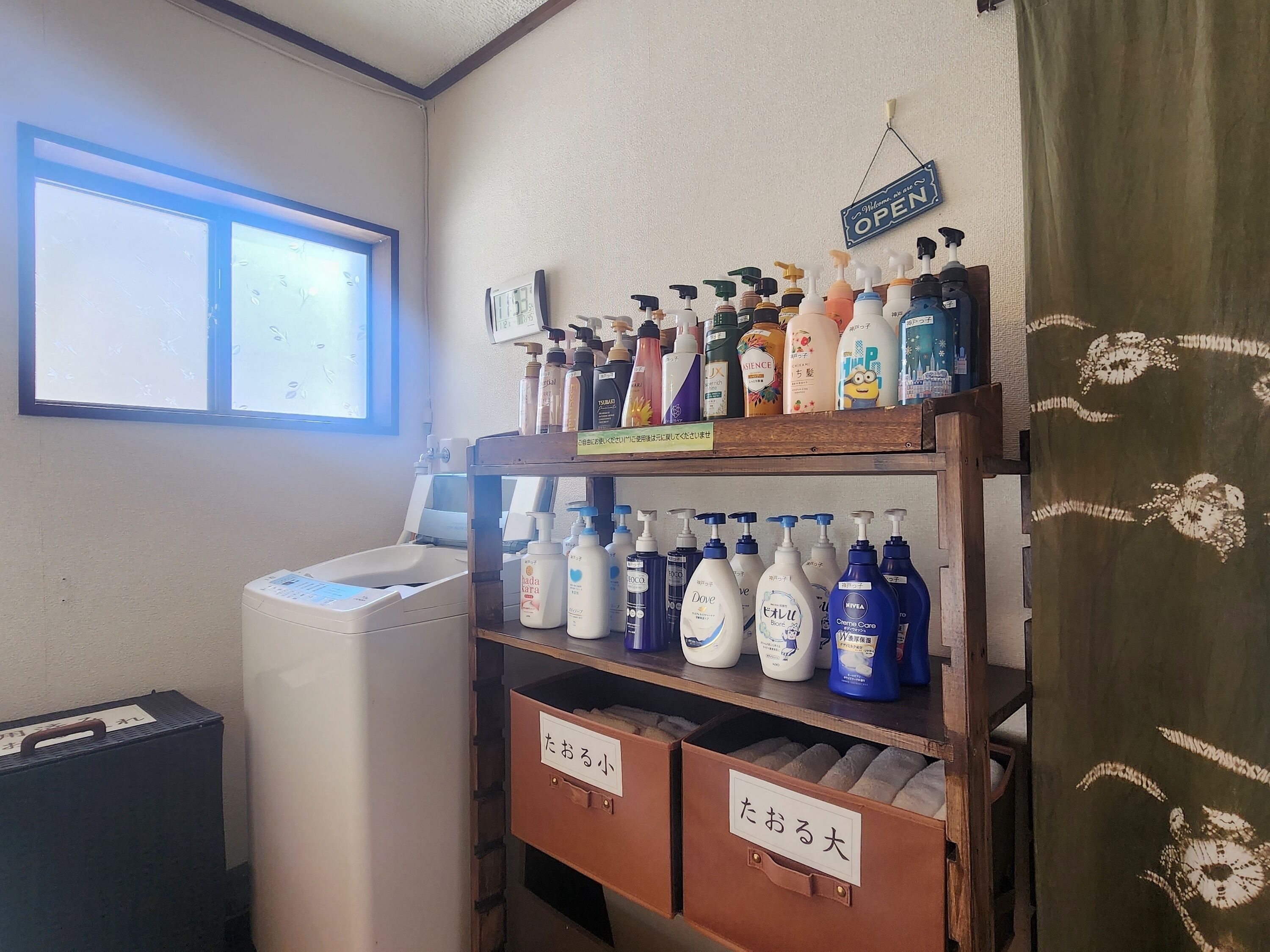 Une salle de bain avec une fenêtre, une étagère contenant divers produits de toilette et des boîtes de rangement étiquetées.