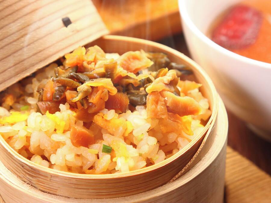 Un panier à vapeur en bambou contenant un plat de riz accompagné de légumes et, éventuellement, de viande.
