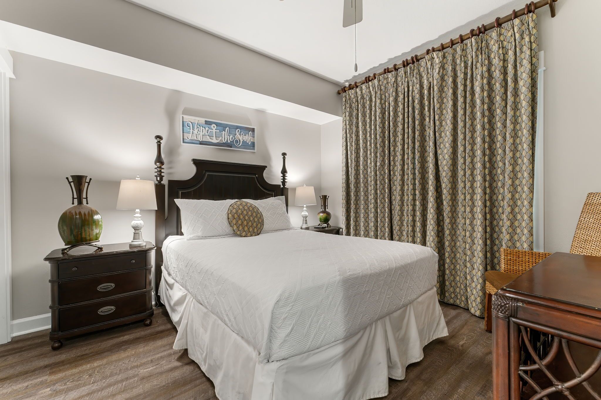 A neatly arranged bedroom with a large bed, two bedside tables with lamps, a decorative wall piece, and a patterned curtain.