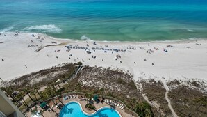 Ett semesterhotell vid stranden med en pool, solstolar, parasoller och utsikt över havet.
