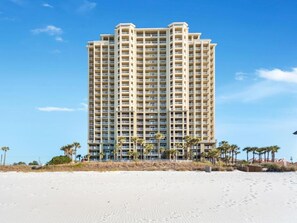 Ein Hochhaus-Hotel mit mehreren Balkonen in der Nähe eines Sandstrandes mit Palmen.