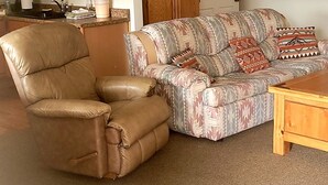 A living room with a brown leather armchair, a patterned sofa, a wooden coffee table, and a ceiling fan. - 5 STAR ESCAPE - Death Valley - Spring Mountain - Prairie Fire Nevada  (Pahrump)