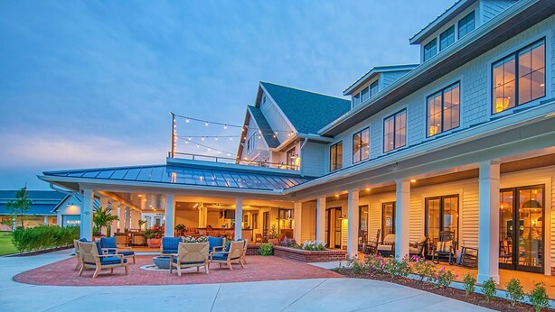 Une maison à deux étages dotée d’un patio couvert, d’un espace salon extérieur et d’une grande baie vitrée.