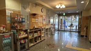A hotel lobby with a vending machine, shelves with various items, a clock, and a clear path leading to the exit. - Step Inn Shin-Osaka Higashiguchi (Osaka)