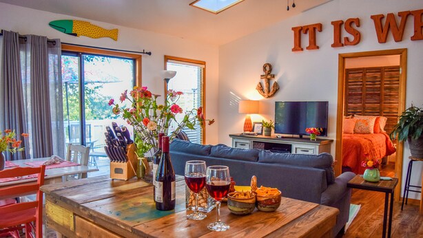 Una sala de estar acogedora con una mesa de centro de madera, un sofá y un televisor. Hay una zona de comedor con una mesa y sillas, y una ventana con cortinas.