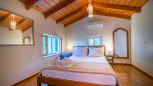 A bedroom with a wooden ceiling, a large bed with white linens, two bedside tables, a mirror, and two windows. - My Little House - Family House with Private Terrace (Aegina)