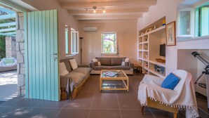 A cozy living room with a sofa, a coffee table, and a bookshelf. - My Little House - Family House with Private Terrace (Aegina)