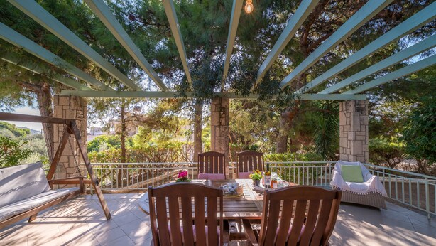 An outdoor patio with a wooden table and chairs, surrounded by stone pillars and a pergola. - My Little House - Family House with Private Terrace (Aegina)