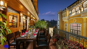 An outdoor dining area with a table set for four, surrounded by wooden chairs, potted plants, and a view of a building. - Sapa Green Hotel (Sa Pa)