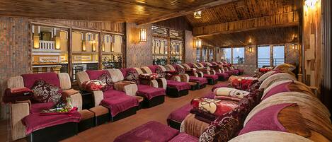 A spa with multiple massage chairs arranged in rows, wooden ceiling, and large windows.