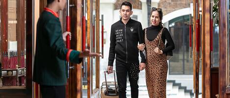 A hotel lobby with a reception desk, a man with a suitcase, and a woman in a leopard print dress.