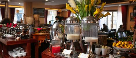 A breakfast bar with coffee machines, a fruit bowl, and a vase with yellow flowers.