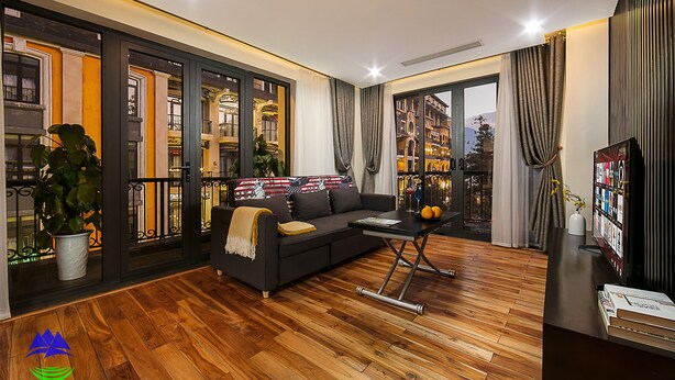 A modern living room with a dark sofa, wooden flooring, and large windows offering city views. - Sapa Green Hotel (Sa Pa)