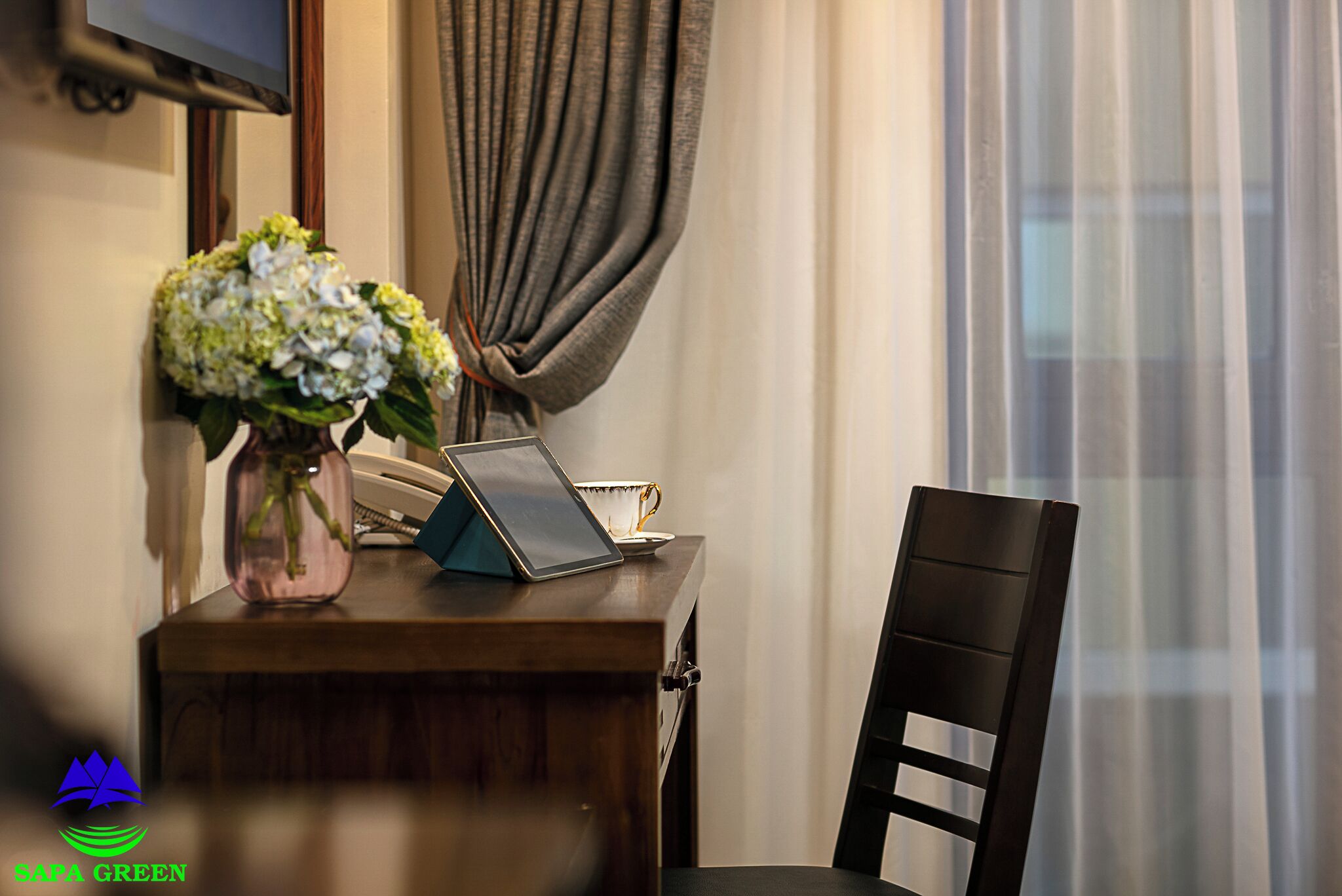 Uma escrivaninha de madeira com um laptop, um vaso de flores e um telefone.